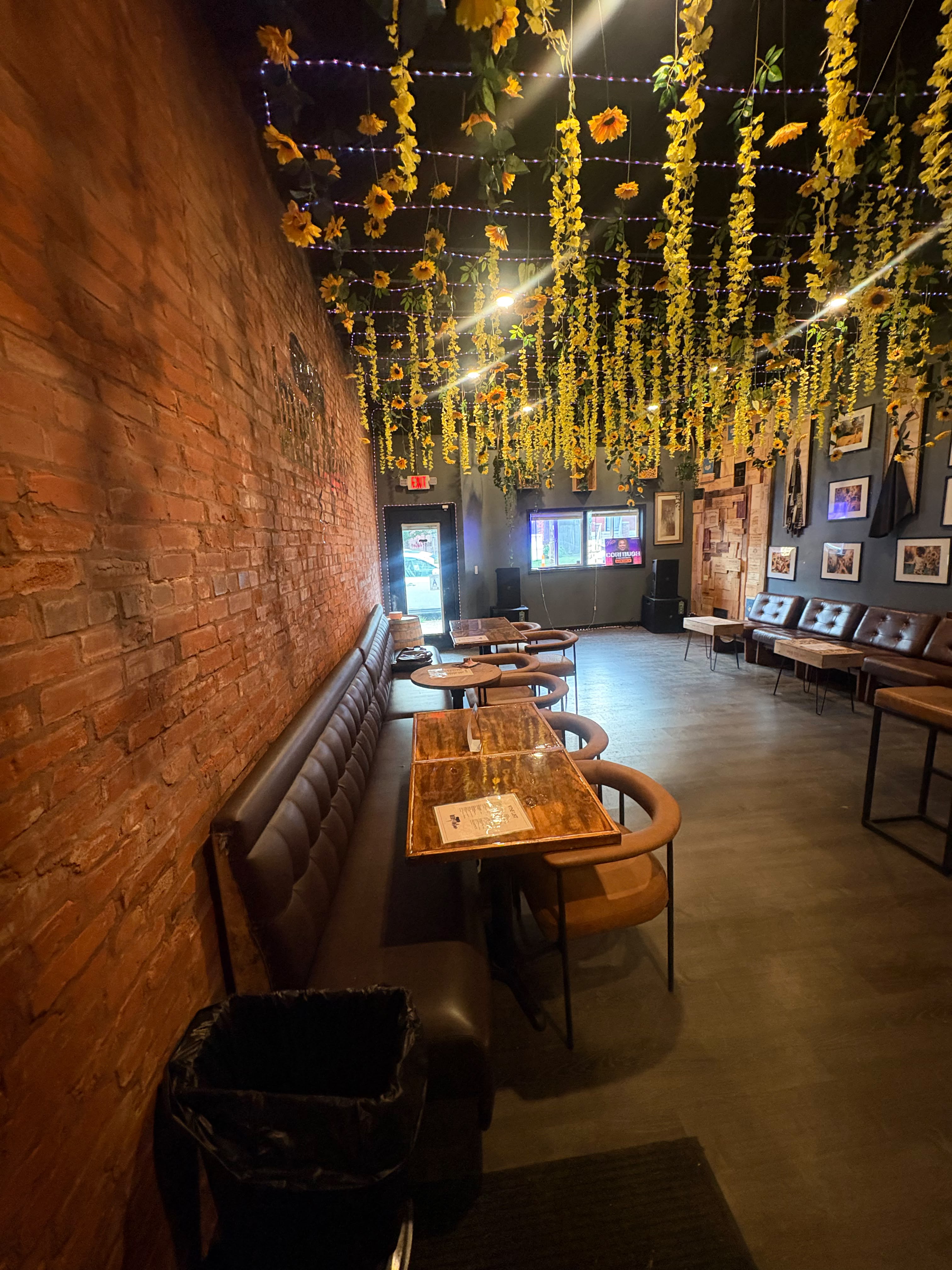 Intertwine's main room — exposed brick, banquette seating, and a sunflower-and-fairy-light ceiling canopy
